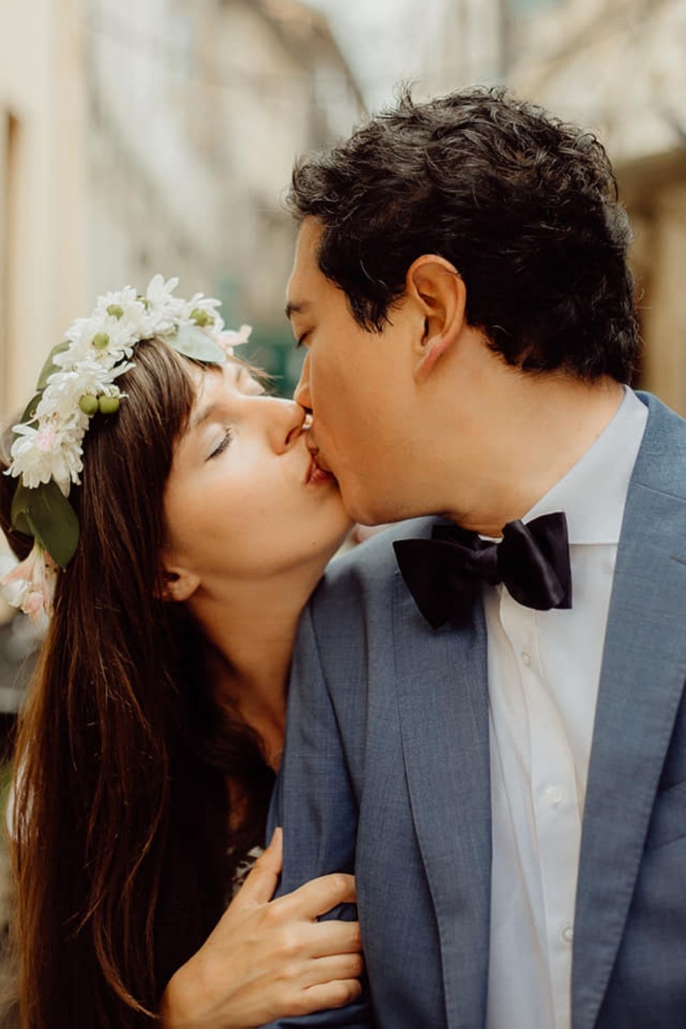 Bride in a head piece kissing groom in blue suit
