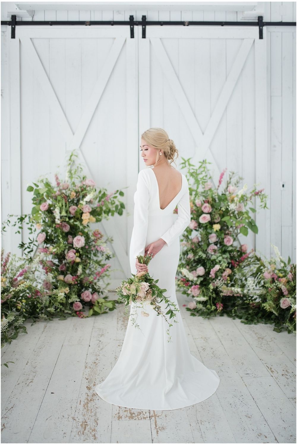 Bride in a white trumpet wedding dress with long sleeves, low back and pink bouquet